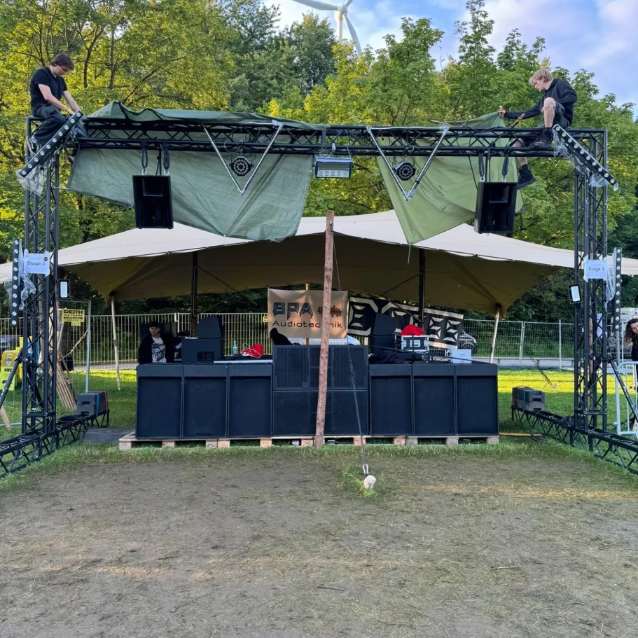 DJ-Pult unter einem Zeltdach, umgeben von Natur, mit Soundtechnik und Licht