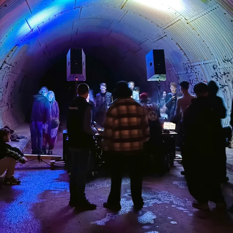 DJ und Zuschauer in einem beleuchteten Tunnel, mit bunt schimmerndem Licht.