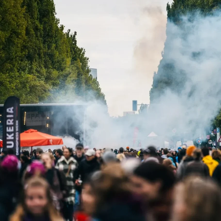 Menschenmenge auf einer Straße, umgeben von Rauch und Ständen.